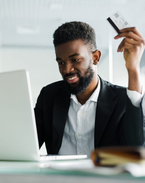 African American man in casual yellow tshirt paying with credit card online while making orders via mobile Internet. Attractive black hipster male making transaction using mobile bank application.